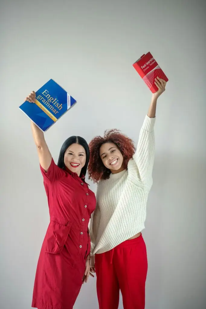 Friends holding English books standing near wall